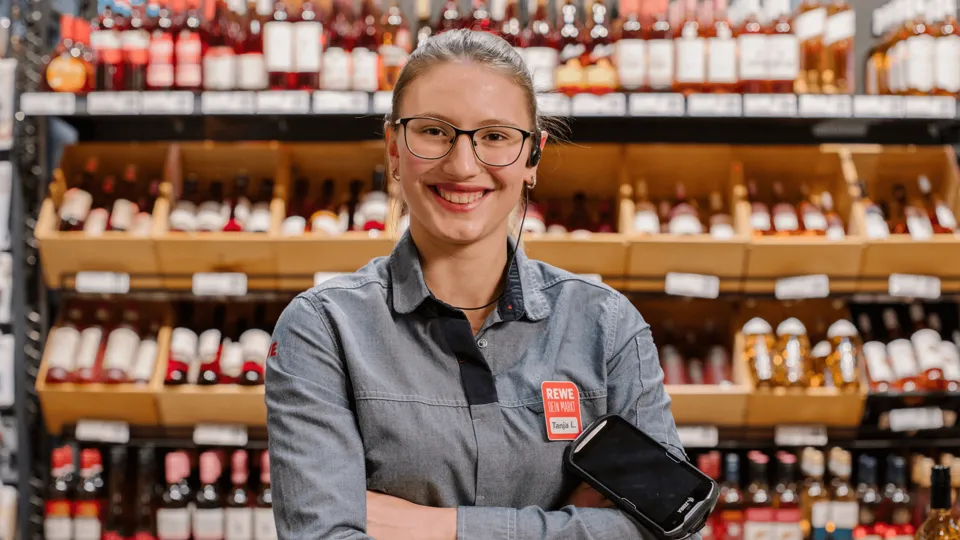 Eine duale REWE Studentin im Handel steht vor einem Weinregal