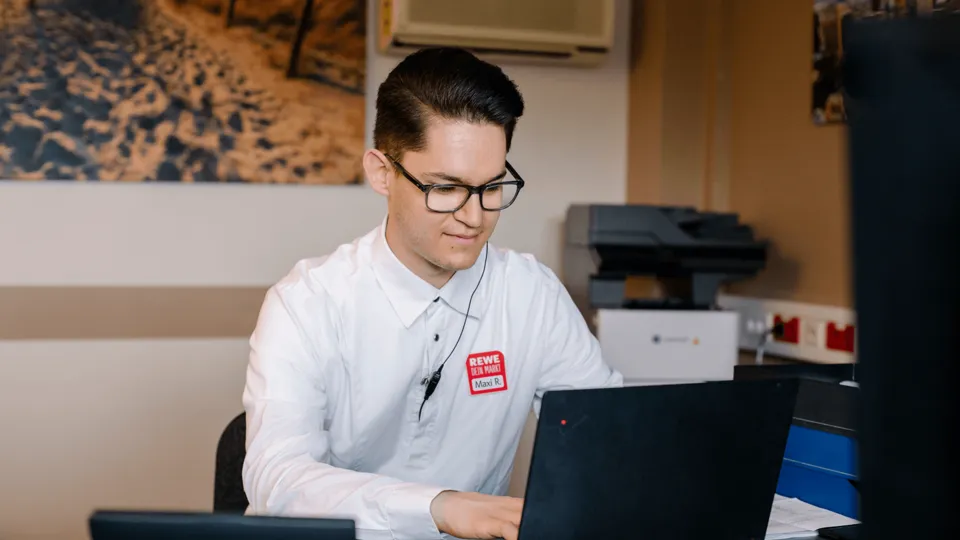 Ein REWE Student im Traineeprogramm zur Selbstaendigkeit als Kaufmann arbeitet an seinem Laptop